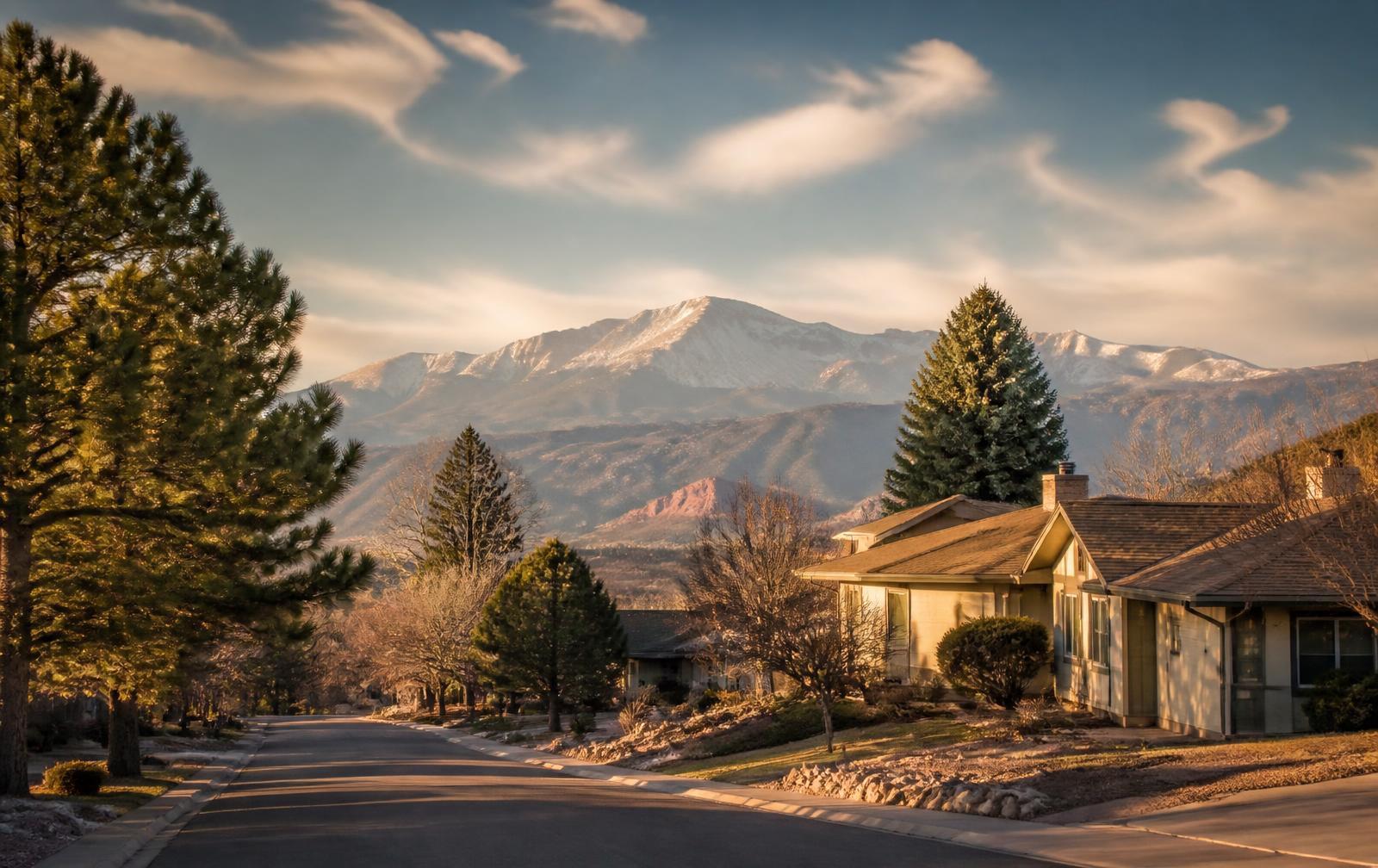 A quiet Colorado Springs neighborhood street with Pikes Peak and the Front Range behind the rooftops at golden hour